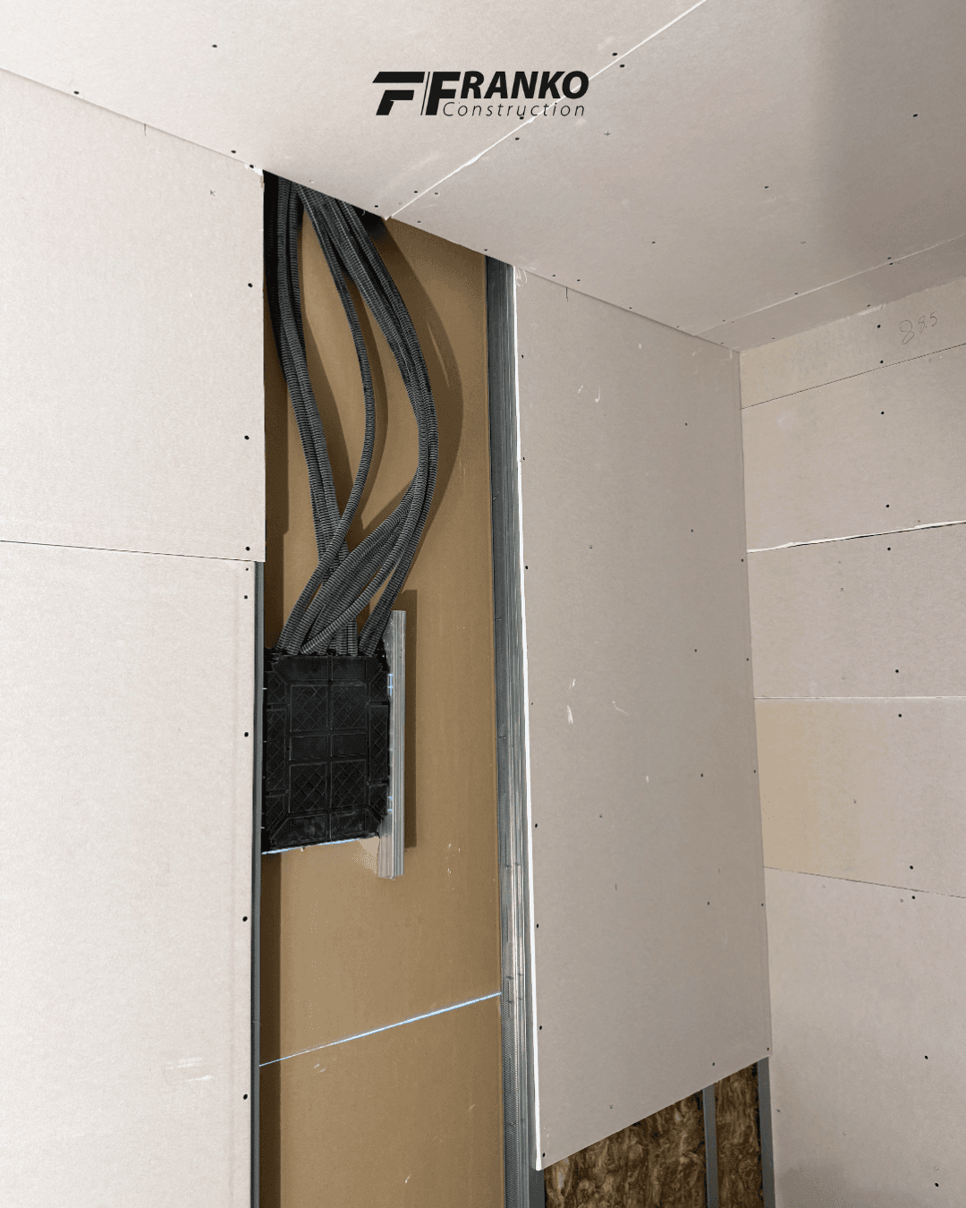 Flexible grey conduits connected to a black electrical box behind partially installed drywall panels.