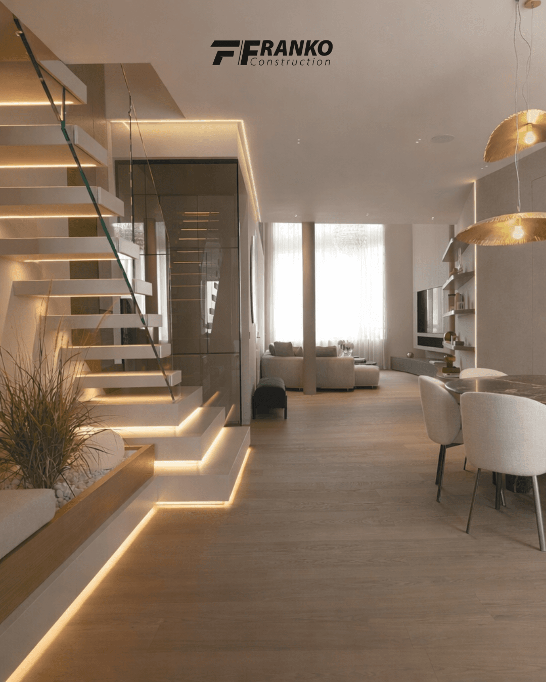 Modern open-plan home featuring an illuminated floating staircase, wooden floors, and warm, neutral-toned furniture.