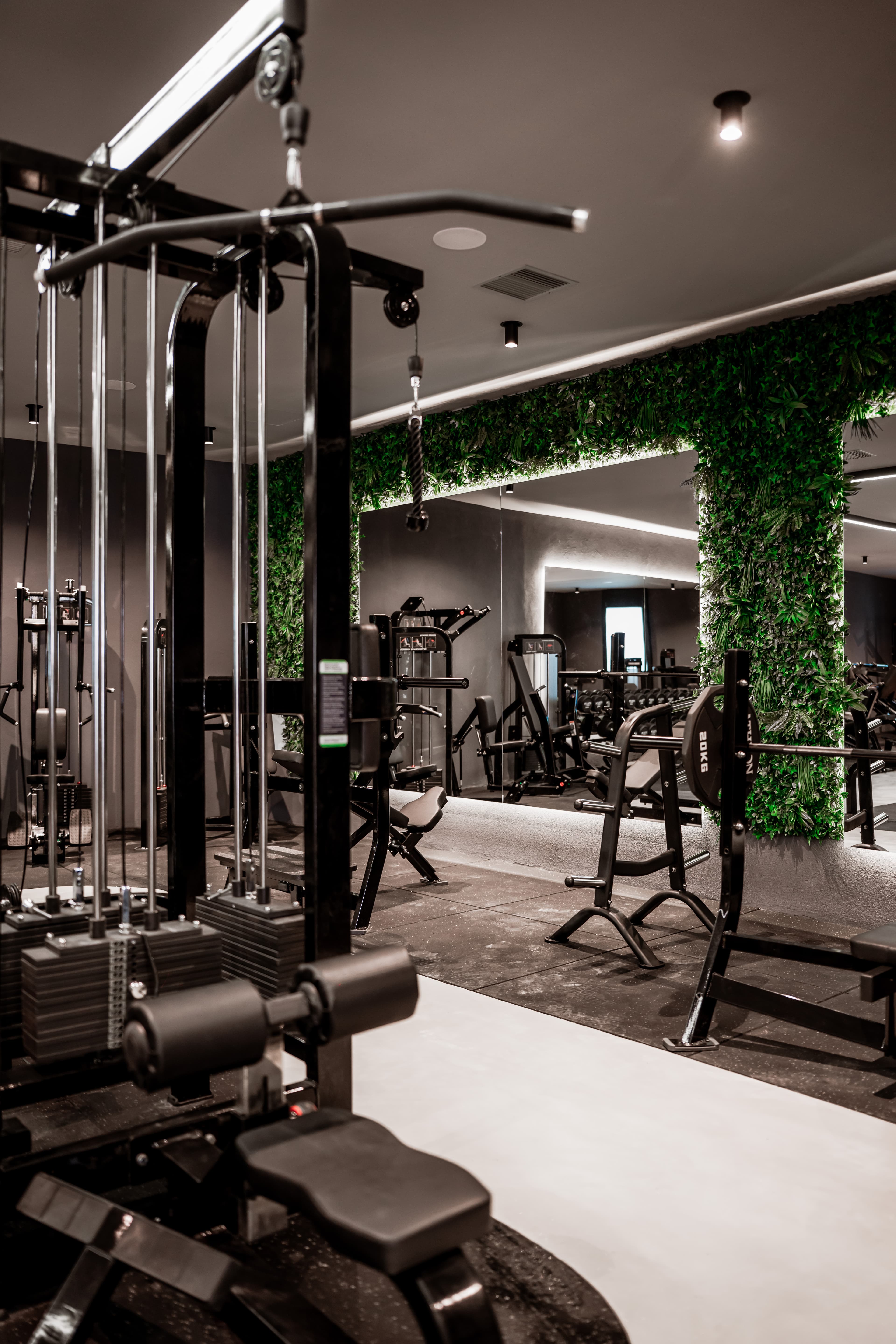 Sleek modern gym featuring black weightlifting equipment, mirrors, and a lush green foliage wall.