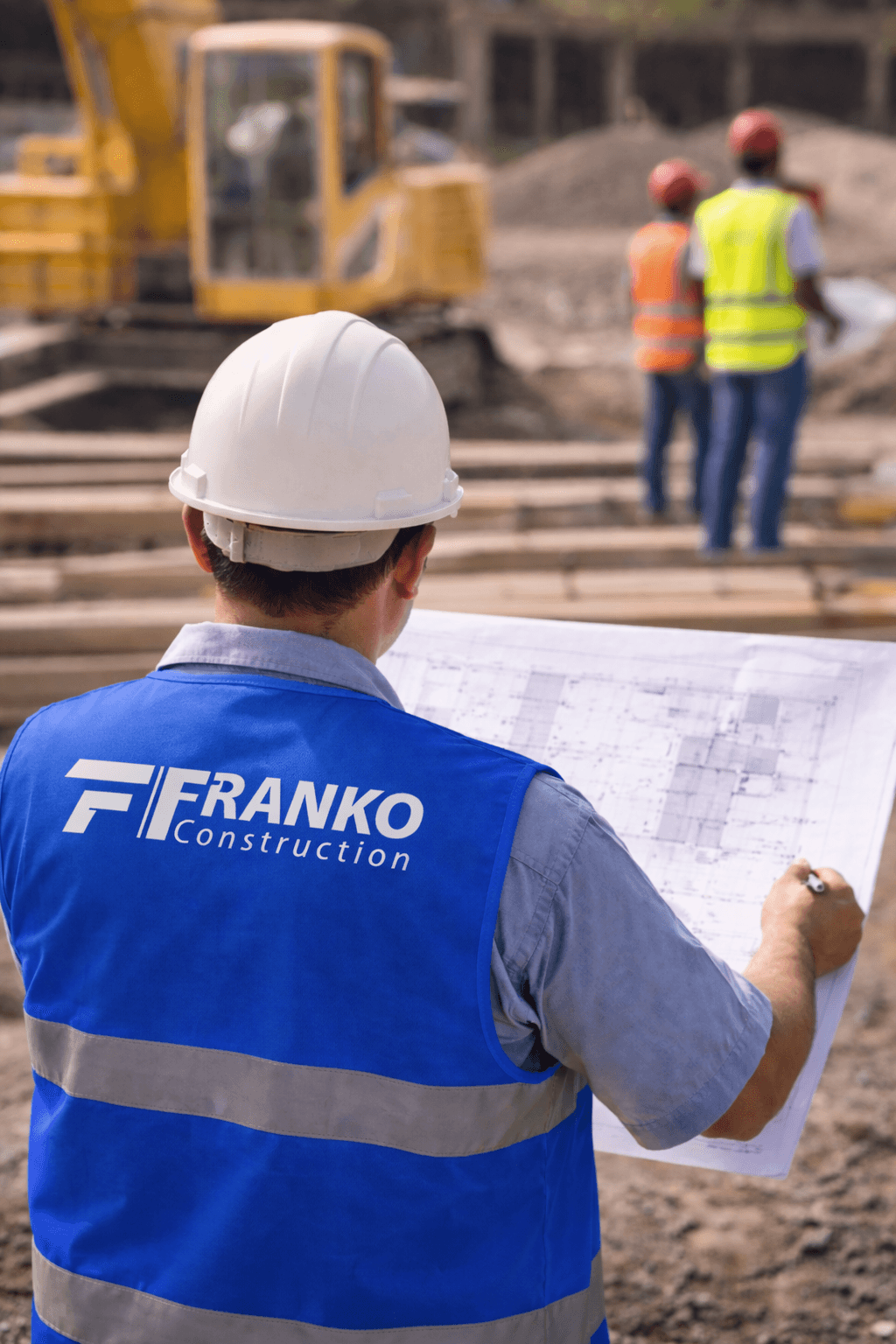 Franko Construction worker in a blue vest reviews blueprints at an active construction site.
