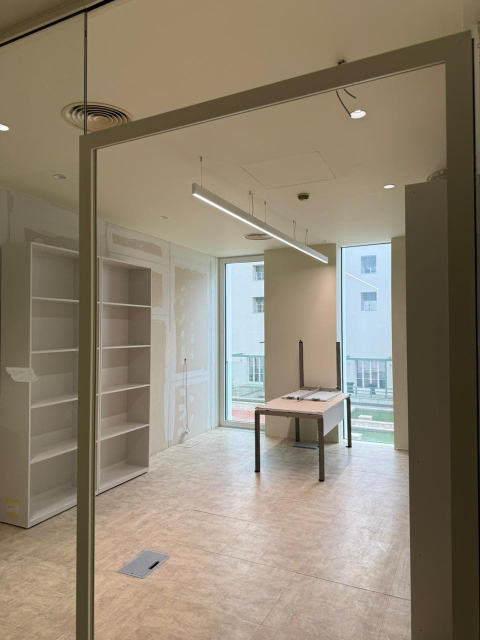 Bright office space under renovation featuring white bookshelves, a desk, and large windows.