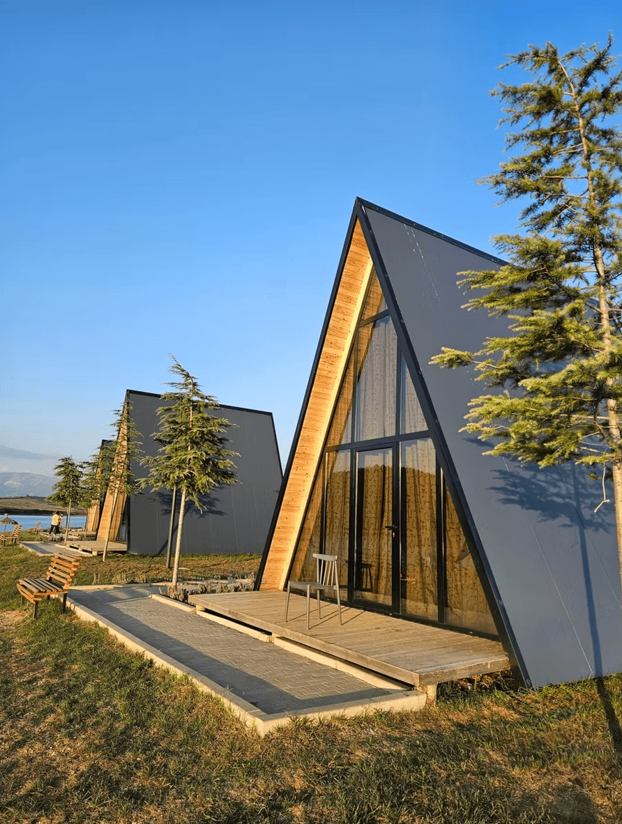 Modern A-frame cabins with large glass windows and wooden decks on a grassy field.