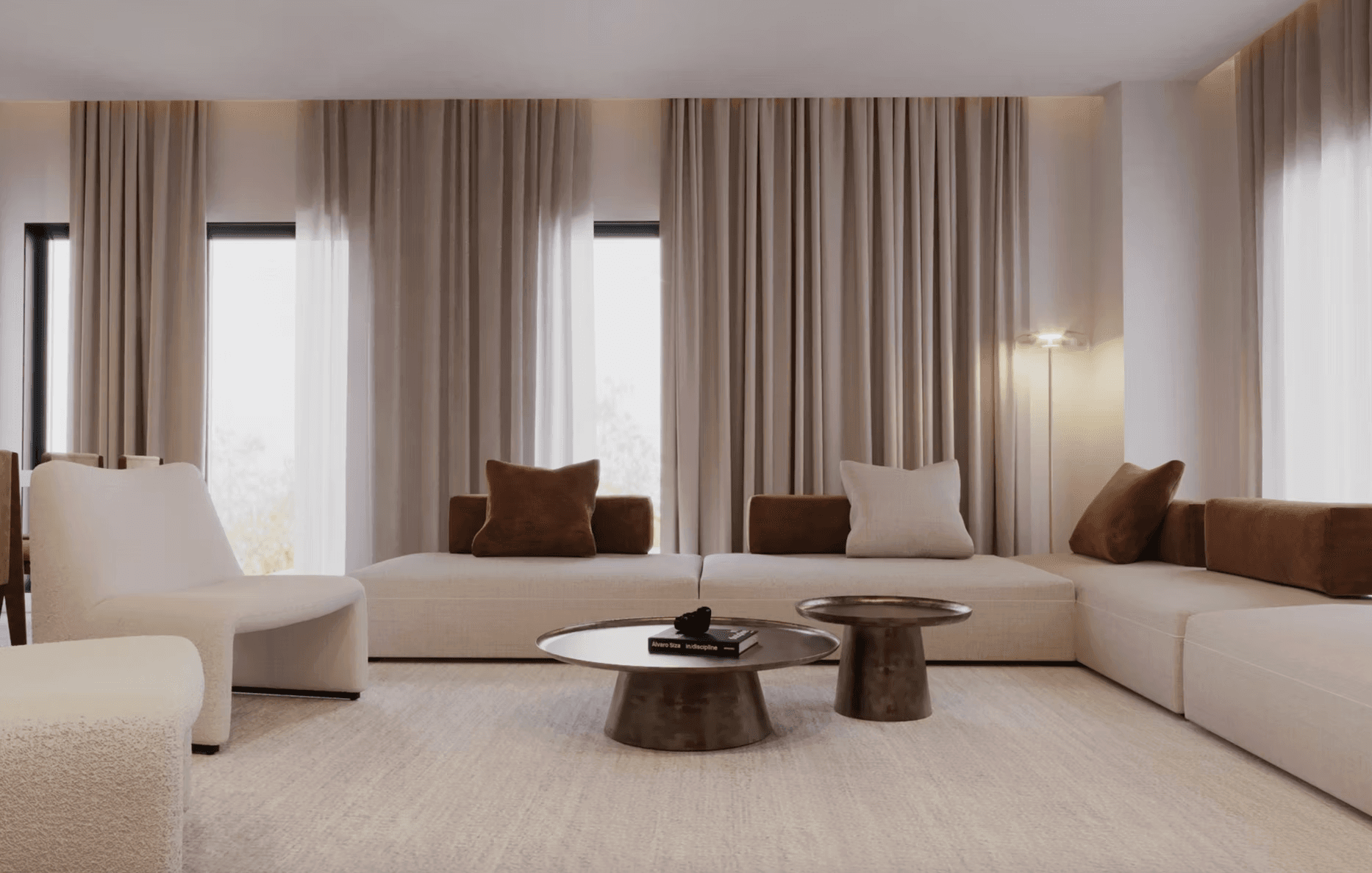 Modern minimalist living room featuring a white sectional sofa, brown pillows, and metallic coffee tables.