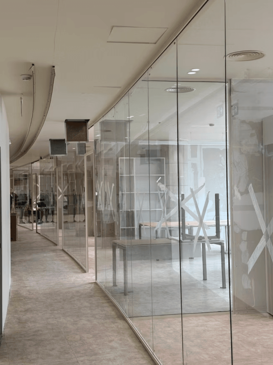 Modern office hallway with glass partitions marked by white tape X's during construction.