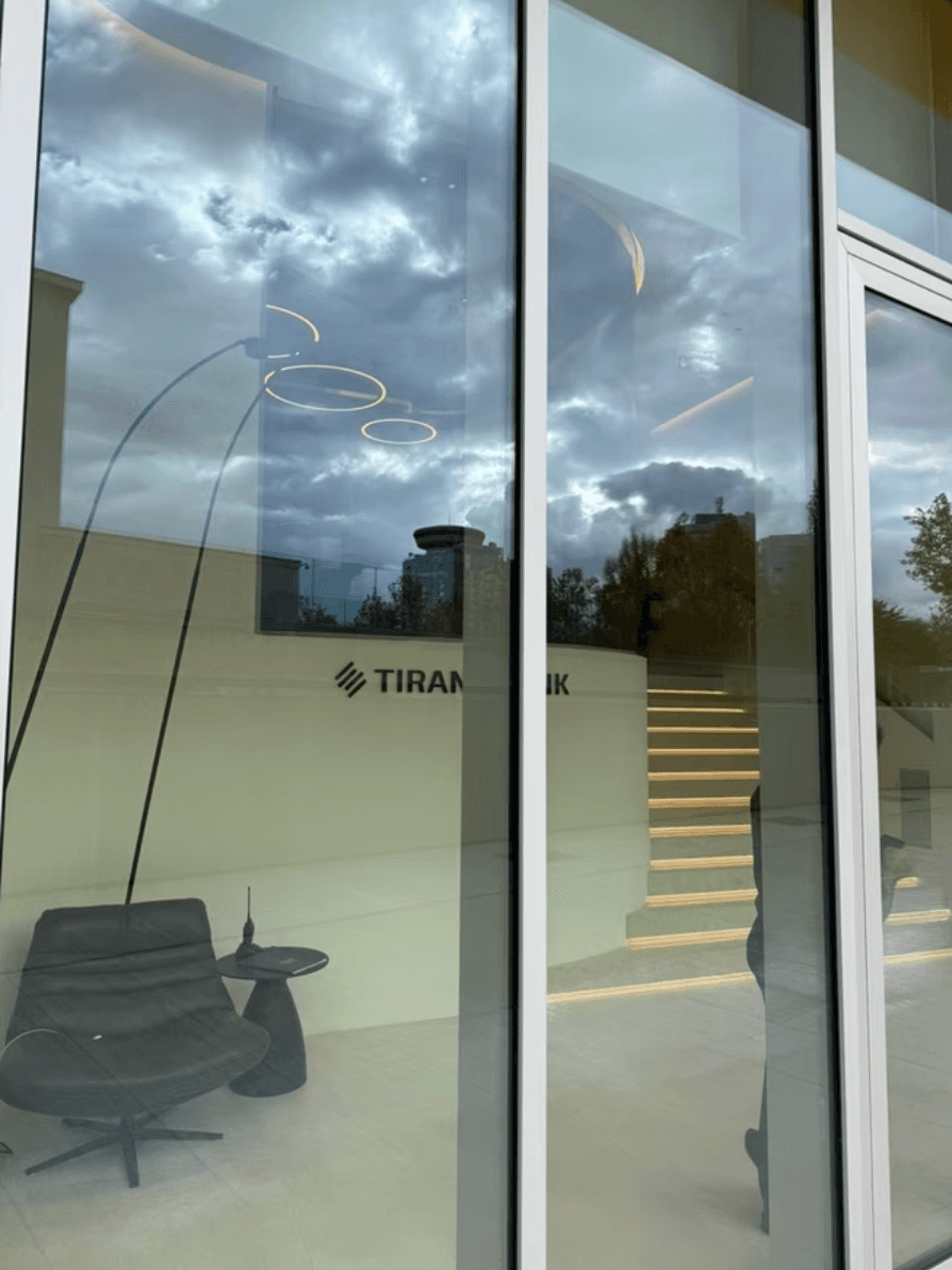 Modern lobby with a black chair and lit stairs, seen through glass reflecting clouds.